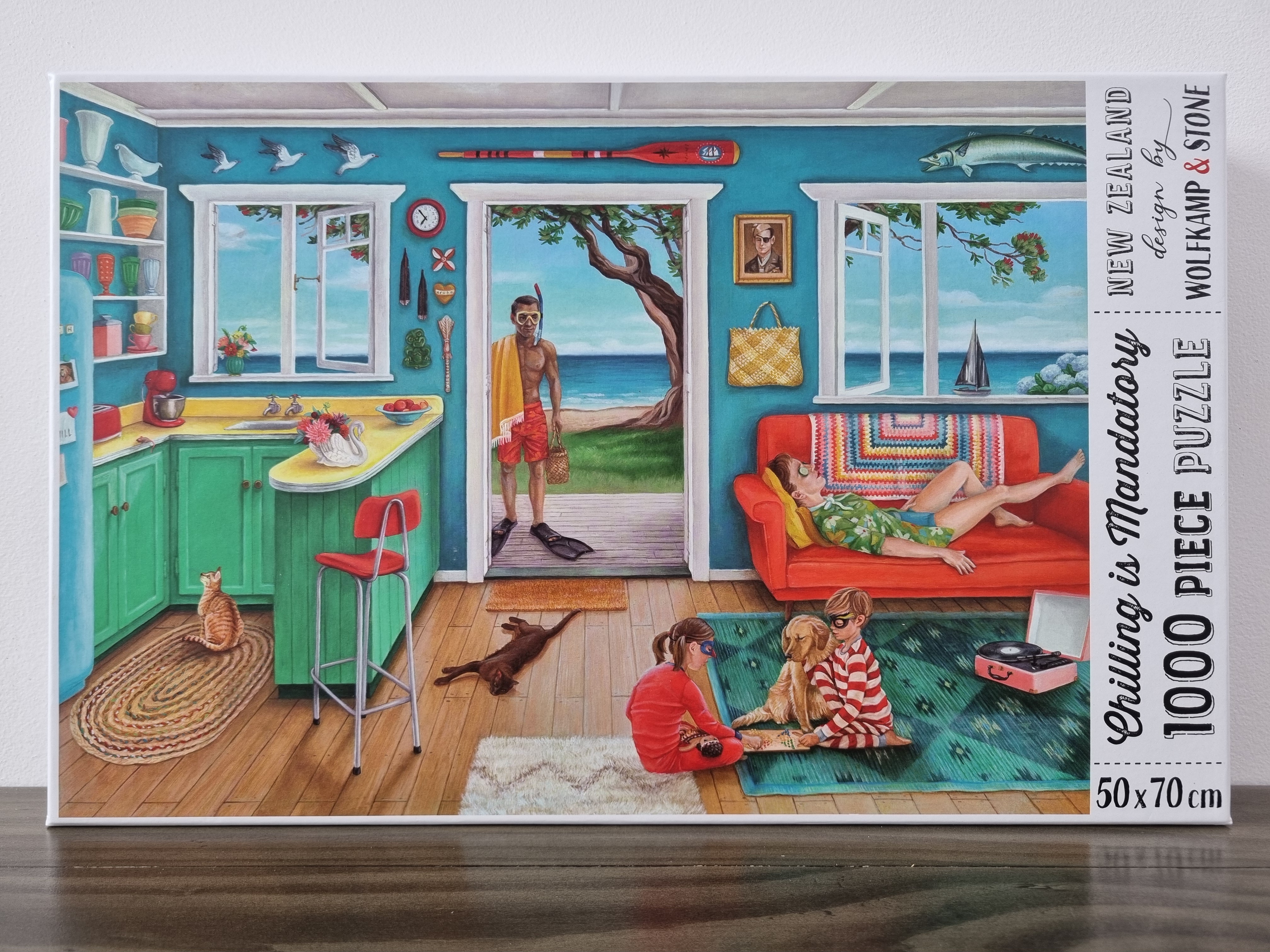A colourful kiwiana 1000 piece puzzle depicting a kiwi classic summer holiday image of a beachfront batch, with a family relaxing and playing. Designed in New Zealand by wolfkamp and stone.