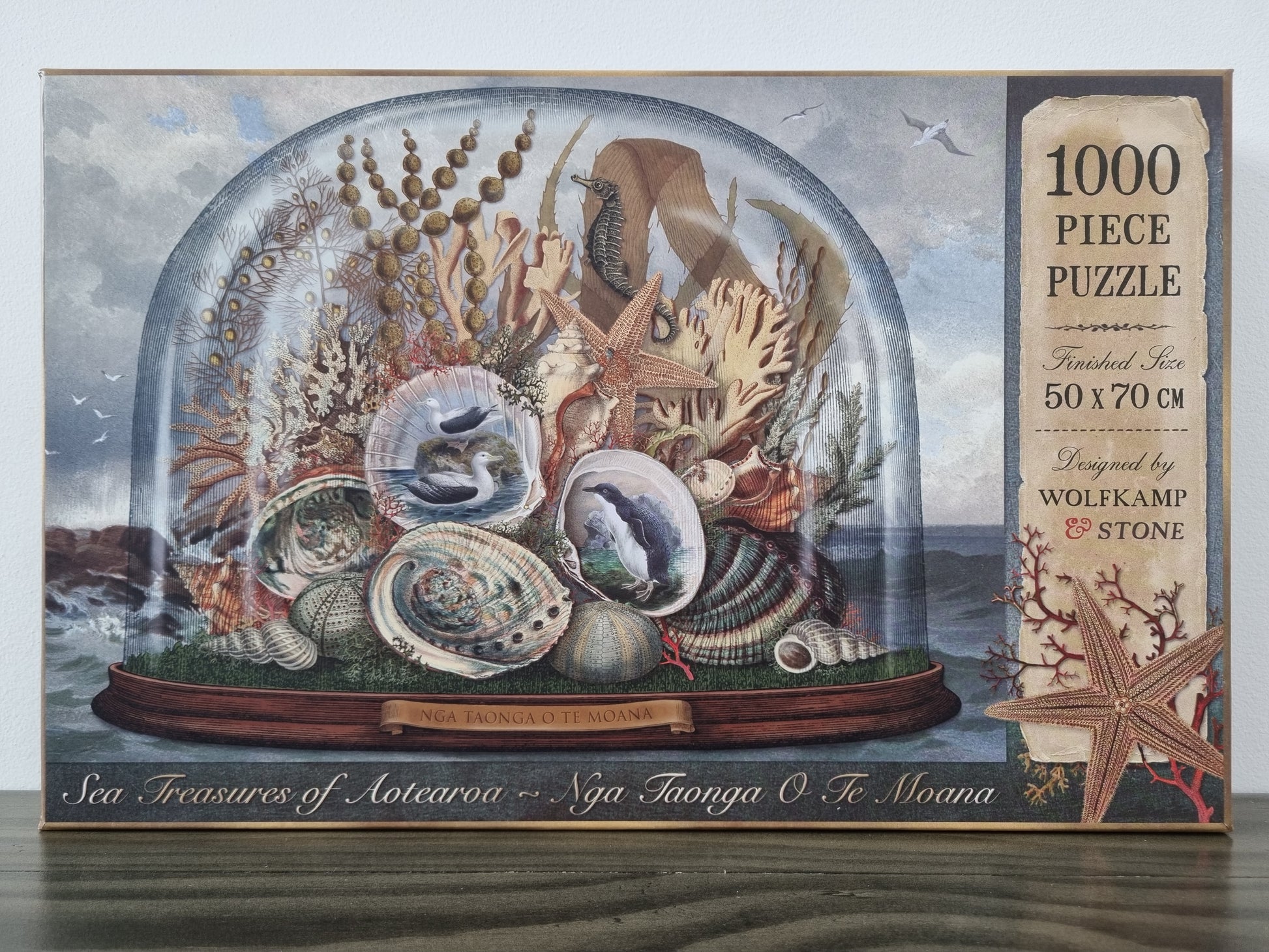 A kiwiana 1000 piece puzzle depicting sea creatures of aotearoa, displayed under a glass dome, designed in new zealand by wolfkamp and stone. 